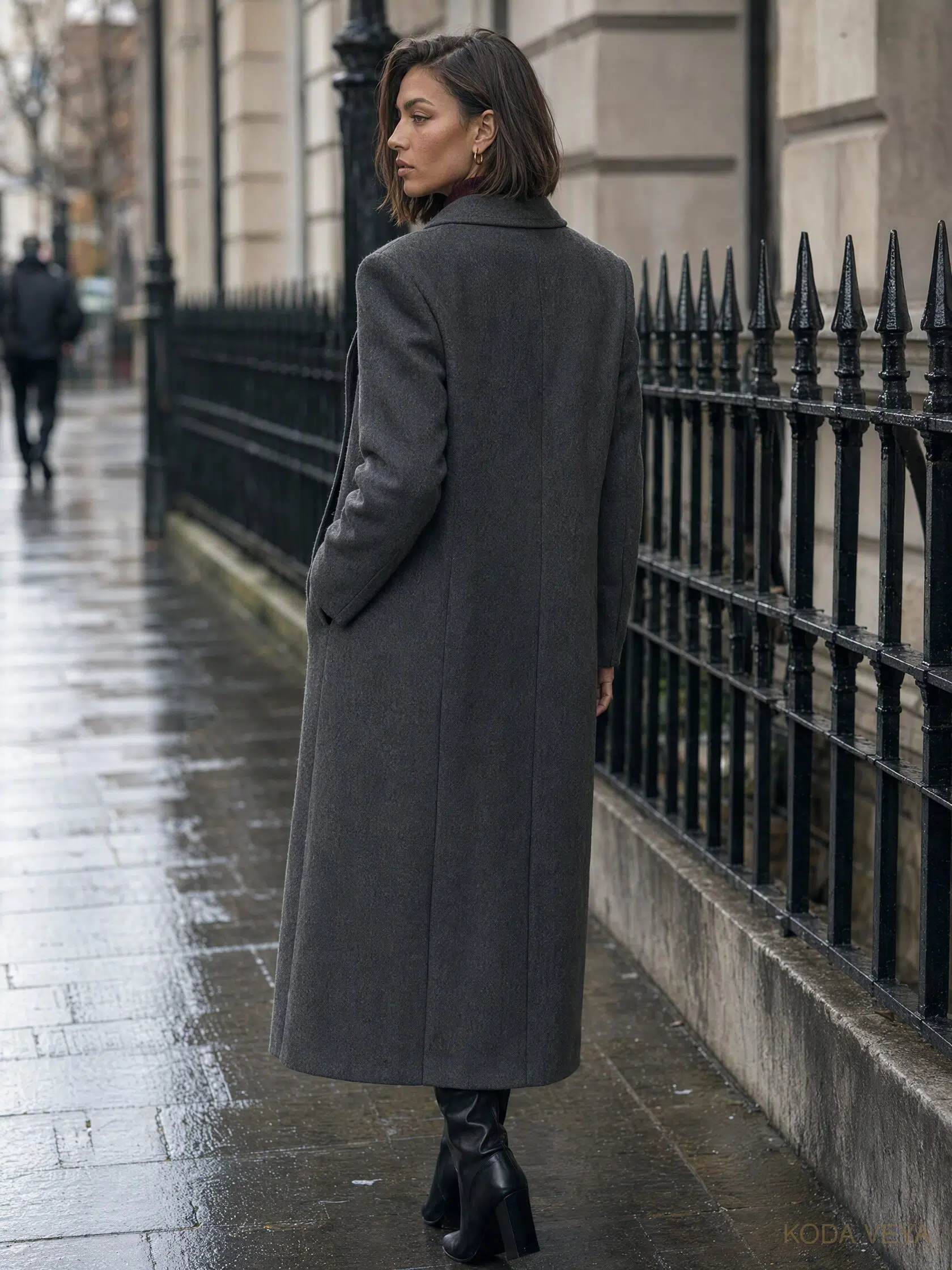 Koda seen from behind on a London street, wearing a long charcoal wool coat with a clean shoulder and back