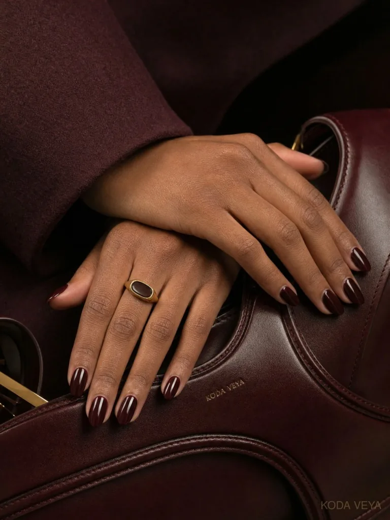 Almost-black burgundy nails on hands resting on a wine leather bag
